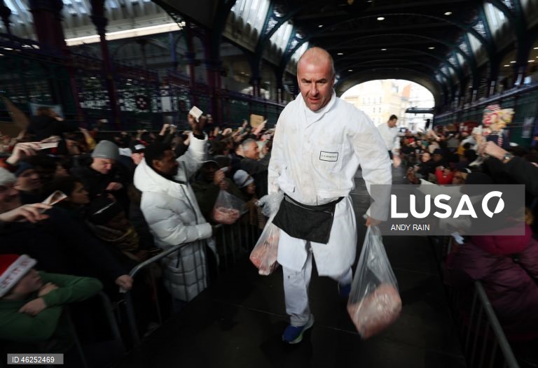 Pessoas observam enquanto talhantes distribuem carne no leilão de carne de Natal em Smithfield, Londres, Grã-Bretanha. Centenas de pessoas reunem-se para ter a oportunidade de comprar carne a preços promocionais na véspera de Natal no mercado de Smithfield, em Londres.