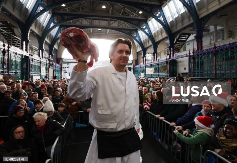 Pessoas observam enquanto talhantes distribuem carne no leilão de carne de Natal em Smithfield, Londres, Grã-Bretanha. Centenas de pessoas reunem-se para ter a oportunidade de comprar carne a preços promocionais na véspera de Natal no mercado de Smithfield, em Londres.