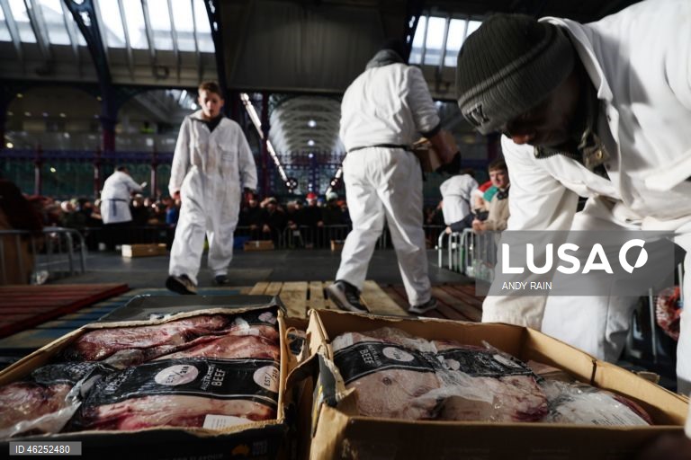 Pessoas observam enquanto talhantes distribuem carne no leilão de carne de Natal em Smithfield, Londres, Grã-Bretanha. Centenas de pessoas reunem-se para ter a oportunidade de comprar carne a preços promocionais na véspera de Natal no mercado de Smithfield, em Londres.