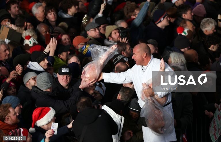 Pessoas observam enquanto talhantes distribuem carne no leilão de carne de Natal em Smithfield, Londres, Grã-Bretanha. Centenas de pessoas reunem-se para ter a oportunidade de comprar carne a preços promocionais na véspera de Natal no mercado de Smithfield, em Londres.