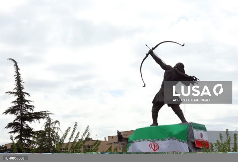 Iranianos passam por um cartaz publicitário de grandes dimensões referente ao Estreito de Ormuz, com a inscrição em persa «Para sempre nas mãos do Irão», numa praça em Teerão, Irão. As tensões entre os Estados Unidos e o Irão continuam, enquanto o Estreito de Ormuz permanece bloqueado.