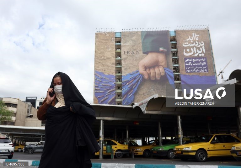 Iranianos passam por um cartaz publicitário de grandes dimensões referente ao Estreito de Ormuz, com a inscrição em persa «Para sempre nas mãos do Irão», numa praça em Teerão, Irão. As tensões entre os Estados Unidos e o Irão continuam, enquanto o Estreito de Ormuz permanece bloqueado.