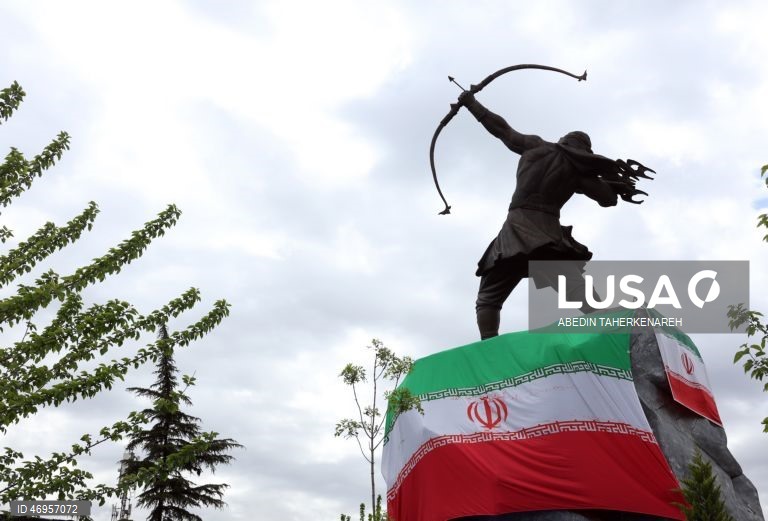 Iranianos passam por um cartaz publicitário de grandes dimensões referente ao Estreito de Ormuz, com a inscrição em persa «Para sempre nas mãos do Irão», numa praça em Teerão, Irão. As tensões entre os Estados Unidos e o Irão continuam, enquanto o Estreito de Ormuz permanece bloqueado.