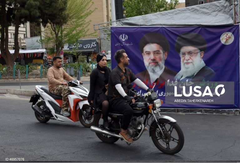 Iranianos passam por um cartaz publicitário de grandes dimensões referente ao Estreito de Ormuz, com a inscrição em persa «Para sempre nas mãos do Irão», numa praça em Teerão, Irão. As tensões entre os Estados Unidos e o Irão continuam, enquanto o Estreito de Ormuz permanece bloqueado.