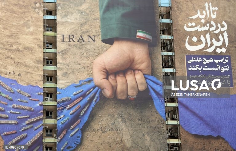 Iranianos passam por um cartaz publicitário de grandes dimensões referente ao Estreito de Ormuz, com a inscrição em persa «Para sempre nas mãos do Irão», numa praça em Teerão, Irão. As tensões entre os Estados Unidos e o Irão continuam, enquanto o Estreito de Ormuz permanece bloqueado.