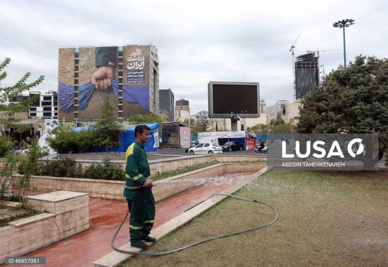 Iranianos passam por um cartaz publicitário de grandes dimensões referente ao Estreito de Ormuz, com a inscrição em persa «Para sempre nas mãos do Irão», numa praça em Teerão, Irão. As tensões entre os Estados Unidos e o Irão continuam, enquanto o Estreito de Ormuz permanece bloqueado.